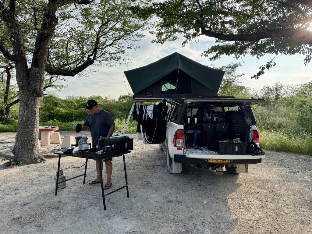 Kamperen met 4x4 en daktent tijdens een selfdrive roadtrip door Namibië, terwijl er buiten wordt gekookt op een camping in Etosha National Park.